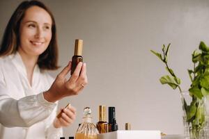 The aromatherapist girl is sitting in her office and holding a bottle of aromatic oils. there are essential oils on the table photo