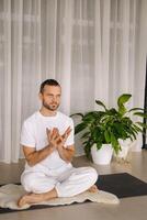 un hombre en blanco ropa de deporte es haciendo yoga con un aptitud habitación. el concepto de un sano estilo de vida foto