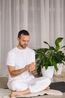 a man in white sportswear is doing yoga with a fitness room. the concept of a healthy lifestyle photo