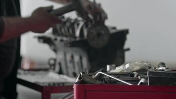 mekaniker reparationer bil motor blockera delar med metall hammare i reparera affär antal fot. video