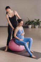 Pregnant woman with a trainer during fitness classes with a ball photo