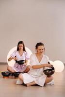 Two female yoga teachers play on Tibetan bowls in the gym during a yoga retreat photo