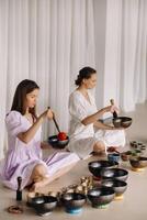 Two female yoga teachers play on Tibetan bowls in the gym during a yoga retreat photo