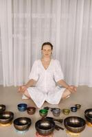 A woman sits with Tibetan bowls in the lotus position before doing yoga in the gym photo