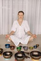A woman sits with Tibetan bowls in the lotus position before doing yoga in the gym photo