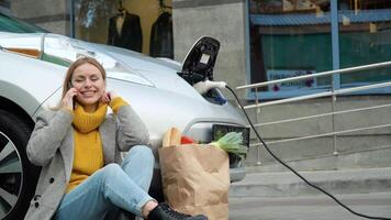 Woman talking on the phone while charging an electric car. Environmentally friendly transport video