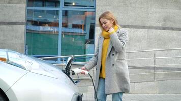 Woman plugging in her electric car to charge near business center. Electrical car recharging video
