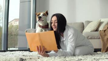 joven mujer es leyendo libro con su perro en hermosa moderno Departamento video