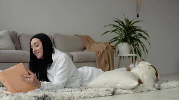 Young woman relaxing with her dog reading a book in a beautiful modern apartment video