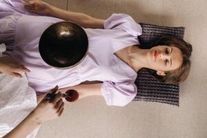 The copper singing bowl of the Nepalese Buddha in the spa. A young beautiful woman is doing a massage with singing bowls in a spa salon against the backdrop of a waterfall photo