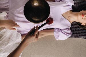 The copper singing bowl of the Nepalese Buddha in the spa. A young beautiful woman is doing a massage with singing bowls in a spa salon against the backdrop of a waterfall photo