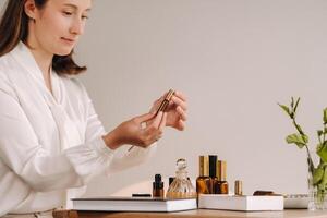 The aromatherapist girl is sitting in her office and holding a bottle of aromatic oils. there are essential oils on the table photo