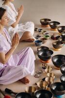 Two women are sitting with Tibetan bowls in the lotus position before a yoga class in the gym photo