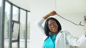 contento joven africano americano mujer médico bailando con un estetoscopio en el hospital video