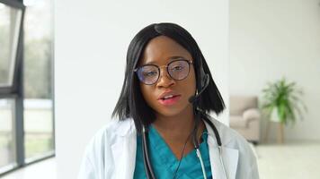 professionell afrikansk amerikan kvinna läkare i vit medicinsk täcka och headsetet framställning konferens ring upp på bärbar dator dator, hört distans patient uppkopplad i video chatt