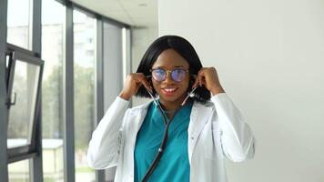 feliz jovem africano americano mulher médico vestindo branco médico casaco e estetoscópio olhando às Câmera. sorridente fêmea médico posando dentro hospital escritório video