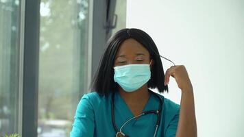 Young african woman doctor in blue protective mask looking at the camera video