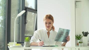 Female doctor studying X-ray scan and writes the result in a notebook. Healthcare, medicine concept video