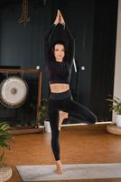 A girl in a black sports uniform does yoga standing on a mat in the gym photo