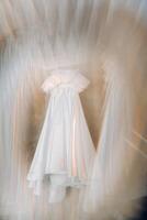 White wedding dress hanging on a hanger in a hotel room photo