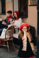 un elegante niña con baguettes soportes cerca el Tienda en contra el antecedentes de su padres foto