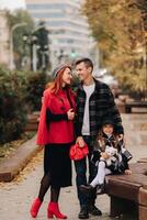 un elegante familia de Tres paseos mediante el otoño ciudad posando para un fotógrafo . papá, mamá y hija en el otoño ciudad foto