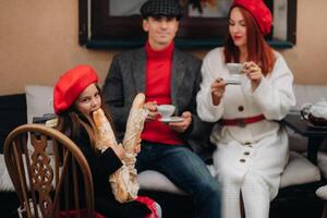un elegante familia de Tres es sentado a un mesa fuera de en un café y Bebiendo café. papá, mamá y hija en el otoño ciudad foto