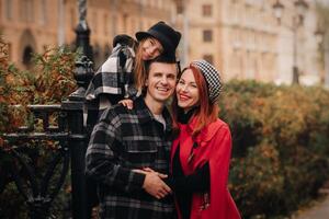 un elegante familia de Tres paseos mediante el otoño ciudad posando para un fotógrafo . papá, mamá y hija en el otoño ciudad foto