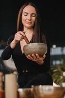 A woman in the lotus position using a singing bowl indoors . Relaxation and meditation. Sound therapy, alternative medicine. Buddhist healing practices photo