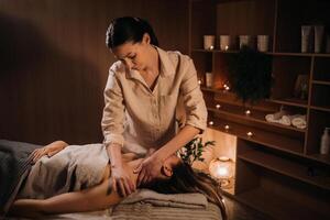 A masseuse gives a body massage to a woman in a spa center. A professional masseur massages the shoulder of a girl lying in a spa center photo