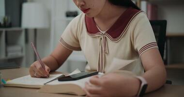 Footage steady shot, Selective focus, Young asian woman sitting at desk writing information on diary notebook while reading book and work on mobile phone at home, creative thoughts to journaling video