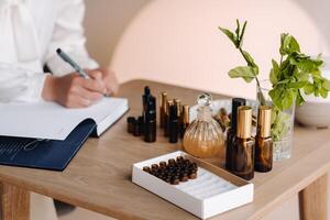 Close-up of female hands holding a bottle of essential oil and writing an entry in a notebook, aromatherapy photo