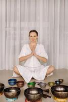 A woman sits with Tibetan bowls in the lotus position before doing yoga in the gym photo