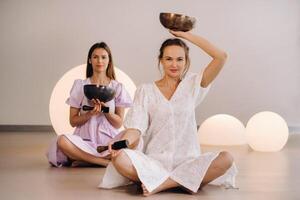 Two female yoga teachers playing a Tibetan bowl in the gym during a yoga retreat photo