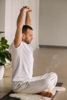 a man in white sportswear is doing yoga with a fitness room. the concept of a healthy lifestyle photo