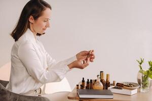 The aromatherapist girl is sitting in her office and holding a bottle of aromatic oils. there are essential oils on the table photo