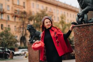 A beautiful stylish woman dressed in an elegant red coat with a stylish red handbag in the autumn city photo