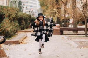 A stylish little girl in a hat walks around the autumn city photo