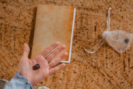 There is a dice in a person's hand. Close-up of a hand with a dice on the background of a notebook photo