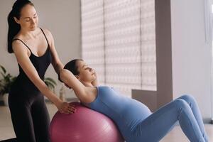 Pregnant woman with a trainer during fitness classes with a ball photo