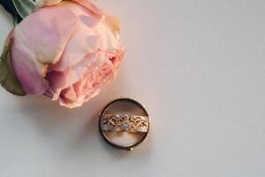 diseñador Boda anillos acostado en el superficie con un Rosa. dos Boda anillos foto
