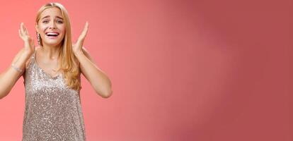 Amazed freaked out excited blond female fan see favorite celebrity star screaming astonished happy look emotive wanna cry happiness waving palms near head thrilled red background photo