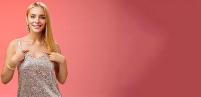 Boastful good-looking confident blond european woman in silver luxurious dress pointing herself smiling proudly bragging talking own accomplishments goals standing red background self-assured photo