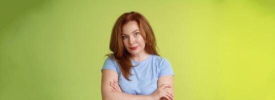 Confused shocked redhead mother look serious worried puzzled cross arms chest self-soothing calming gesture stare camera perplexed frustrated bad son behaviour stand green background disappointed photo