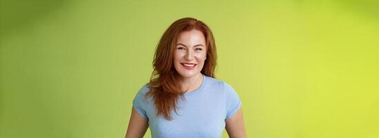 Cheerful kind happy redhead middle-aged mother look caring delighted smiling broadly gaze admiration joy stand blue t-shirt green background amused enthusiastic expression photo