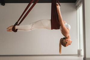 A girl in white sportswear does yoga on a hanging hammock in the fitness room photo