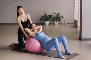 Pregnant woman with a trainer during fitness classes with a ball photo
