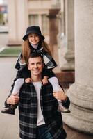 A cheerful Daughter is sitting on dad's shoulders and walking around the autumn city photo