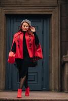 un hermosa elegante mujer vestido en un elegante rojo Saco con un elegante rojo bolso en el otoño ciudad foto