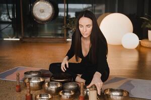 un mujer en el loto posición utilizando un canto cuenco adentro . relajación y meditación. sonido terapia, alternativa medicamento. budista curación practicas foto